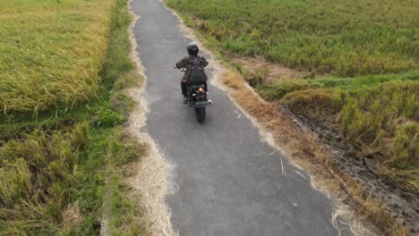 Biker-guy-driving-a-motorbike-in-a-rice-field-area-with-mountain-views-with-rural-atmosphere