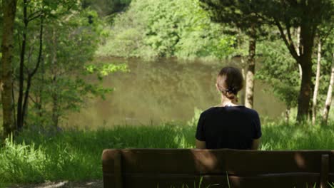 Una-Mujer-Solitaria-Se-Sentó-En-Un-Banco-Mirando-El-Lago-Fangoso-En-El-Fondo-Del-Valle-Rodeado-De-Naturaleza-Y-árboles