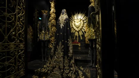 Dolce-Y-Gabbana,-Lujosas-Y-Ornamentadas-Figuras-Misteriosas-Con-Capas-Se-Alzan-Ante-Un-Corazón-Ornamentado-Decorado-En-Oro,-Creando-Una-Atmósfera-Solemne-Y-Teatral.