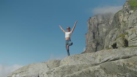 Woman-performs-yoga-tree-position-on-rocky-coast,-front-slow-motion-view