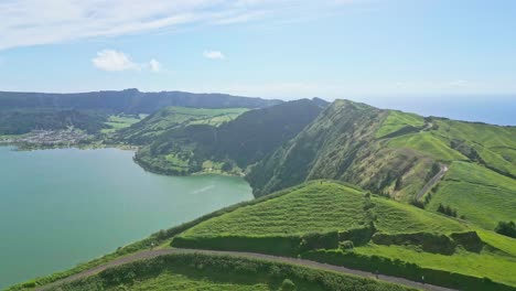 Vista-Aérea-Panorámica-De-Exuberantes-Colinas-Verdes-Y-Un-Sereno-Lago-En-Un-Día-Soleado