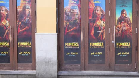 Los-Peatones-Pasan-Por-Un-Cine-Cuyas-Puertas-Están-Decoradas-Con-Carteles-Publicitarios-De-La-Película-Furiosa:-La-Saga-Mad-Max,-Una-Película-De-Acción-Post-apocalíptica-Dirigida-Y-Producida-Por-George-Miller.