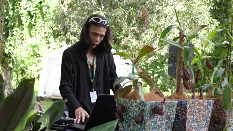 Dj-Sound-Technician-In-Garden-Setting-Sound-Using-Laptop-With-Plant-Pots-Around