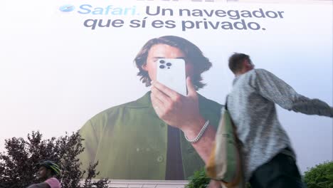 Captados-Desde-Un-ángulo-Bajo,-Peatones-Pasan-Junto-A-Un-Destacado-Cartel-De-Apple-Que-Destaca-Las-Características-De-Privacidad-Del-Navegador-Web-Safari,-Del-Gigante-Tecnológico-Multinacional-Estadounidense.