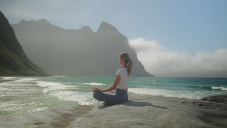 Young-beautiful-blonde-meditating-on-Norway-coastline,-orbiting-view