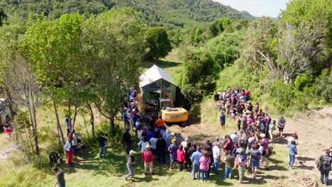 Aerial-View-Of-Excavator-And-Large-Local-Community-Helping-To-Move-House-Across-River-In-Chiloe,-Chile