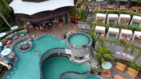 People-Relaxing-at-Luxury-Day-Club-Pool-of-Cretya-Ubud-in-Bali,-Drone-View