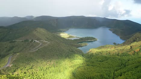 Lagoa-do-fogo-surrounded-by-lush-green-hills-under-a-partly-cloudy-sky,-aerial-view