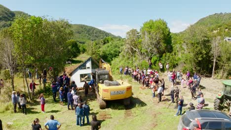 Aerial-View-Of-Excavator-And-Large-Local-Community-Helping-To-Move-House-In-Chiloe,-Chile