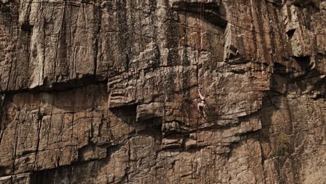 Powerful-woman-climbing-extremely-dangerous-rock-wall,-aerial-view