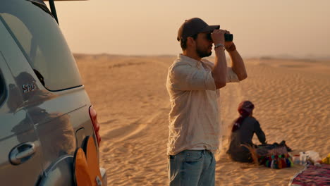 Man-Using-Binoculars-in-the-Desert-standing-next-to-an-offroad-vehicle