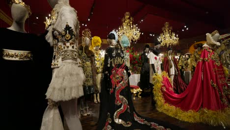 Dolce-And-Gabbana-Luxurious-and-ornate-costumes-on-mannequins-showcased-in-a-red-walled-exhibition-room,-exuding-a-sense-of-opulence-and-artistic-flair
