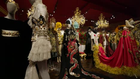 Dolce-&amp;-Gabbana-Luxuriöse-Und-Kunstvolle-Kostüme-Auf-Schaufensterpuppen-In-Einem-Ausstellungsraum-Mit-Roten-Wänden,-Die-Ein-Gefühl-Von-Opulenz-Und-Künstlerischem-Flair-Ausstrahlen