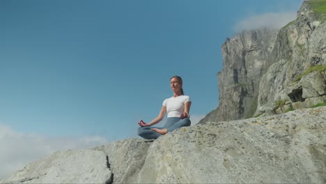 Fit-woman-meditating-on-rocky-coast,-view-from-below-and-ascends
