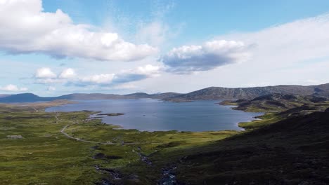 Panoramic-view-of-Nødre-Rjupa-River-in-Beitostølen,-Norway,-with-surrounding-mountains-and-vast-landscape-under-a-blue-sky-with-clouds