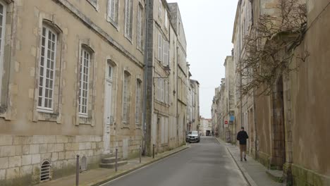 Hombre-Caminando-Por-Una-Calle-Estrecha-Entre-Edificios-Antiguos-En-El-Centro-Histórico-De-La-Rochelle-En-Francia