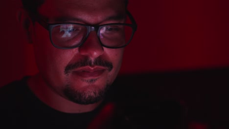 Adult-Hispanic-man-with-glasses-watching-mobile-phone-in-dark-room