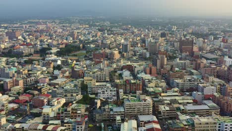 Aerial-descending-shot,-drone-flyover-the-neighborhood-capturing-the-urban-cityscape-of-residential-and-commercial-buildings-in-Douliu-city,-Yunlin-County,-Taiwan-at-sunset