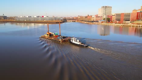 Tugboat-and-Barge-steaming-down-the-Maumee-River,-in-downtown-Toledo,-Ohio,-USA