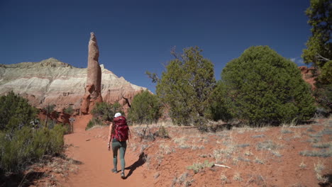 Lonely-Female-Hiker-on-Hiking-Trail-in-Desert-Landscape-Under-Red-Rock-Spire-Sandstone-Formation,-Slow-Motion