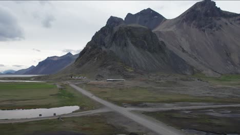 Aerial-shot-of-a-rental-car-driving-through-Stokksnes-with-mountains-in-the-background-in-Iceland-during-summer