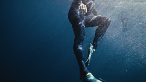 Legs-of-person-wearing-wetsuit-snorkeling-underwater-near-surface-in-clear-ocean