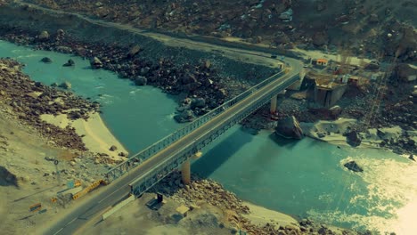 A-stunning-aerial-view-capturing-a-bridge-spanning-a-blue-river-amidst-rugged,-rocky-terrain