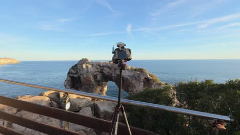 Camera-On-Travel-Tripod-Facing-The-Sea-With-View-Of-Es-Pontas-Natural-Arch-In-Mallorca,-Spain
