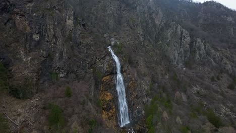 Aerial-view-of-a-majestic-waterfall-cascading-down-a-steep,-rocky-cliff-amidst-a-rugged-mountain-landscape