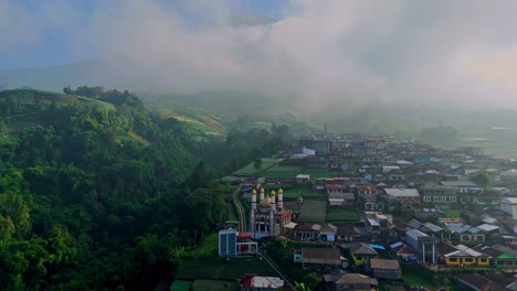 Vista-Aérea-De-Un-Hermoso-Pueblo-Con-Una-Montaña-Brumosa-Al-Fondo