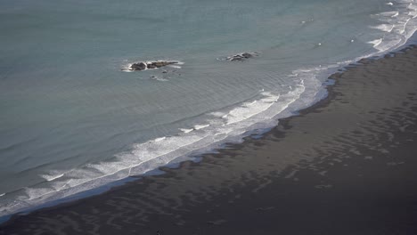 Waves-crashing-on-a-black-sand-beach-made-of-volcanic-rock-in-Stokksnes,-Iceland-during-summer