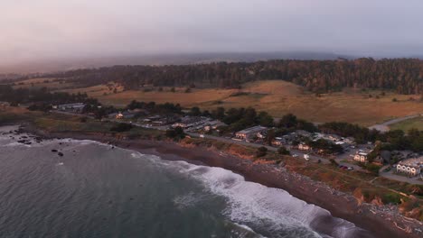 Aerial-wide-descending-shot-of-oceanfront-inns-lining-Moonstone-Beach-at-sunset-in-Cambria,-California