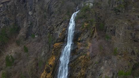 Drone-close-up-shot-of-a-stunning-waterfall-cascading-down-a-rocky-cliff-surrounded-by-green-trees