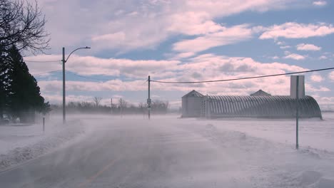 Snow-storm-blizzard,-frozen-road-in-rural-field-near-farm,-powerful-wind,-Canada