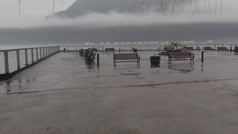 Rainy-foggy-atmospheric-day-on-the-cold-spring-New-York-waterfront,-with-benches-and-a-freight-train-crossing-across-the-river