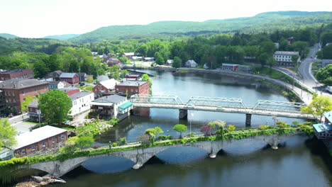 Scenic-aerial-overview-of-quaint-American-countryside-and-river-with-towns-connected-by-the-iconic-Bridge-of-Flowers-in-Shelburne-Falls,-Massachusetts