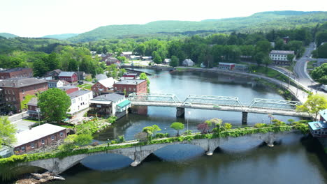 Panorama-Aéreo-Panorámico-De-La-Pintoresca-Campiña-Americana-Y-El-Río-Con-Pueblos-Conectados-Por-El-Icónico-Puente-De-Flores-En-Shelburne-Falls,-Massachusetts