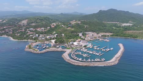 Aerial-wide-shot-of-marina-ocean-world-and-green-tropical-mountain-landscape-in-background