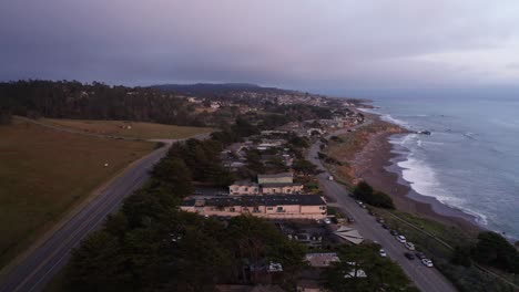 Low-aerial-shot-flying-over-oceanfront-inns-along-Moonstone-Beach-at-sunset-in-Cambria,-California