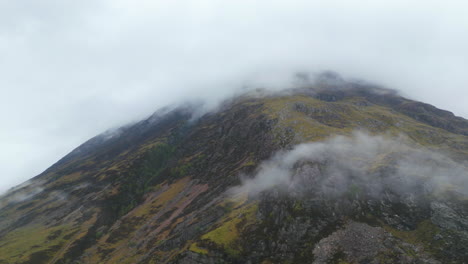 Aerial-circling-mountain-top-covered-in-mist,-Glen-Coe,-Scotland