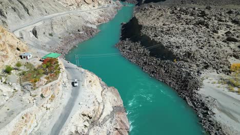 Aerial-view-of-a-beautiful-turquoise-river-flowing-through-a-rocky-mountain-terrain-with-a-winding-road-and-rugged-landscape-under-a-clear-sky