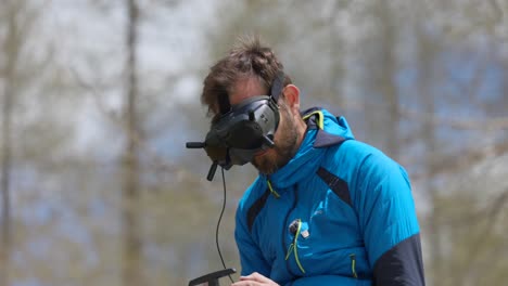 Man-in-blue-jacket-using-a-virtual-reality-headset-and-remote-control-to-navigate-a-drone-in-an-outdoor-setting