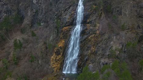 Aerial-view-of-a-towering-waterfall-cascading-down-a-steep,-rocky-cliff-surrounded-by-lush-greenery