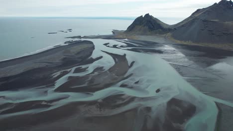 Aerial-view-of-the-colorful-blue-glacier-rivers-delta-near-Stokksnes-in-Iceland-during-summer,-showcasing-the-vibrant-hues-and-intricate-river-patterns