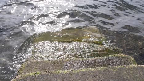 Ocean-waves-water-with-beautiful-sunlight-lapping-onto-coastal-steps-in-Oban,-Scotland-UK