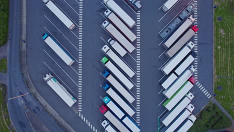 Aerial,-top-down-moving-shot-of-trucks-parked-on-a-parking-lot-near-a-highway-in-Belgium