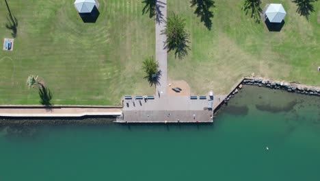 Drone-top-down-rises-above-coastal-promenade-and-park-on-Lake-Illawarra-Windang-NSW