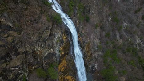 Drone-aerial-view-of-a-wonderful-waterfall-cascading-down-a-steep-rocky-cliff-in-local-mountain-area