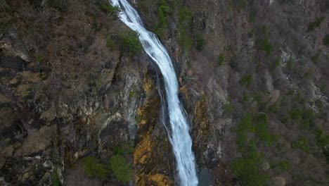 Vista-Aérea-De-Drones-De-Una-Maravillosa-Cascada-Que-Cae-Por-Un-Empinado-Acantilado-Rocoso-En-Una-Zona-Montañosa-Local