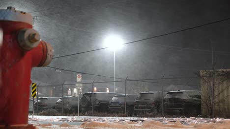 Snow-storm-low-level-video-of-red-fire-hydrant-next-to-car-park-at-night
